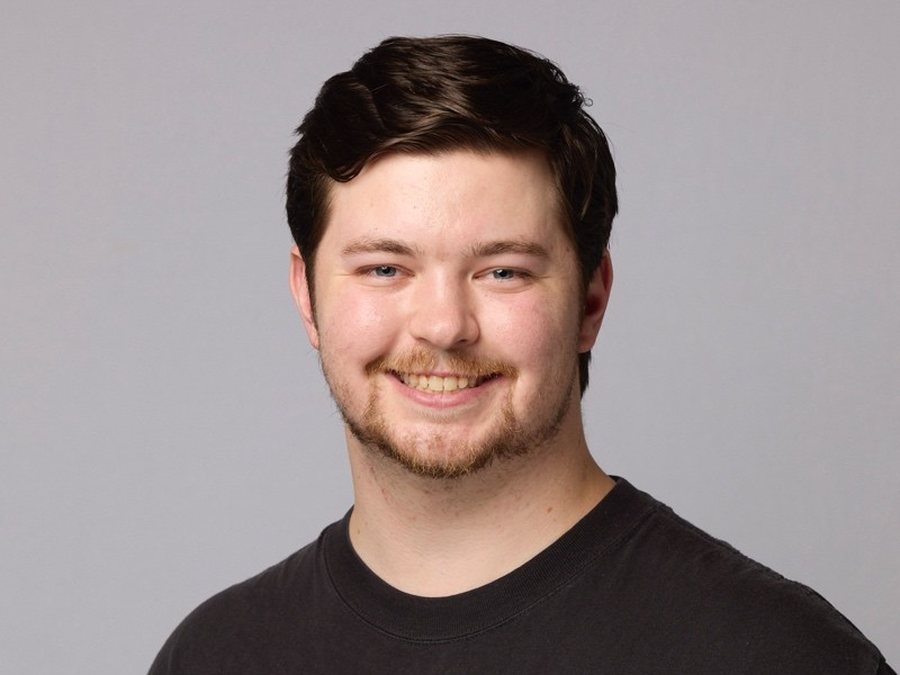 Tobias smiling in a dark t-shirt against a grey background